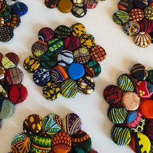 May include: A set of colourful coasters made from bottle caps covered in patterned fabric. The coasters are arranged in a flower shape and feature a variety of colours and patterns.