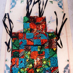 Peut inclure: Un porte-bébé en tissu patchwork coloré avec des sangles noires. Le tissu est composé de différents motifs et couleurs, dont le rouge, l'orange, le jaune, le vert, le bleu et le noir.