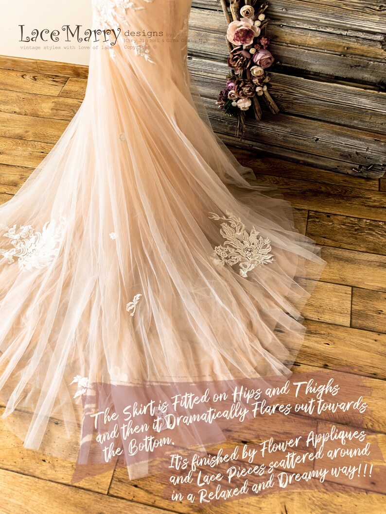 May include: A close-up of a blush-colored tulle wedding dress with delicate white lace appliques. The skirt is fitted on the hips and thighs and then flares out dramatically towards the bottom. The text "The Shirt is Fitted on Hips and Thighs and then it Dramatically Flares out towards the Bottom. It's finished by Flower Appliques and Lace Pieces scattered around in a Relaxed and Dreamy way!!!" is written on the dress.