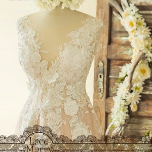 May include: A white lace wedding dress with a V-neckline and floral embroidery. The dress is on a mannequin and has a sheer overlay.