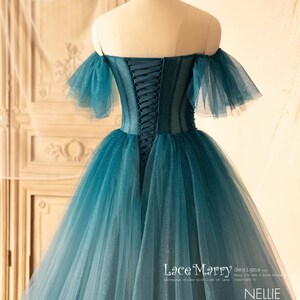 K&ouml;nnte beinhalten: Ein blaues T&uuml;ll-Ballkleid in Teal mit einem herzf&ouml;rmigen Ausschnitt und schulterfreien &Auml;rmeln. Das Kleid hat einen Schn&uuml;rr&uuml;cken und einen glitzernden Ombre-Effekt.