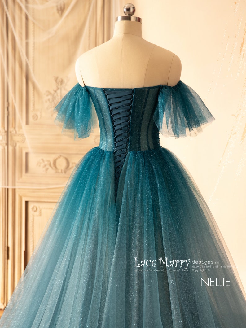 K&ouml;nnte beinhalten: Ein blaues T&uuml;ll-Ballkleid in Teal mit einem herzf&ouml;rmigen Ausschnitt und schulterfreien &Auml;rmeln. Das Kleid hat einen Schn&uuml;rr&uuml;cken und einen glitzernden Ombre-Effekt.