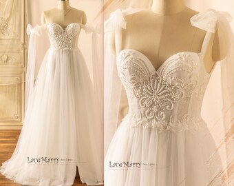 May include: A white tulle wedding dress with a sweetheart neckline and a fitted bodice. The bodice is adorned with intricate beaded lace embroidery. The dress has off-the-shoulder straps with tulle bows. The dress has a flowing A-line skirt. "LaceMarry designs" is written on the bottom of the dress.