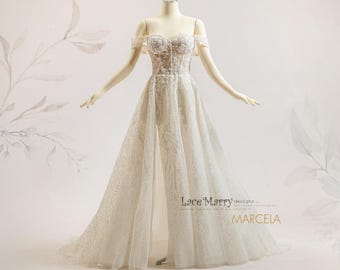May include: A white off-the-shoulder wedding gown with intricate lace detailing. The bodice features a sweetheart neckline and a fitted design, while the skirt flows into a split front, revealing a layer of fabric underneath. The dress is displayed on a mannequin.