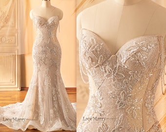 May include: A strapless, beaded wedding dress with a fitted bodice and a flowing skirt. The dress is made of a sheer fabric with delicate floral embroidery and sequins. The dress is shown on a mannequin.