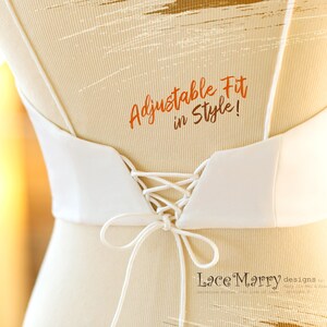 Pu&ograve; includere: Un corpetto da sposa bianco con schienale a lacci. Il corpetto ha una scollatura a V ed &egrave; regolabile. Il testo "Adjustable Fit in Style!" &egrave; scritto in arancione sul retro del corpetto. Il testo "LaceMarry designs by" &egrave; scritto in nero nella parte inferiore dell'immagine.