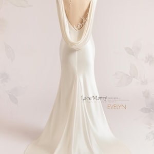 Pu&ograve; includere: Un abito da sposa in satin bianco con schiena scoperta e un pannello trasparente con delicati ricami floreali. L'abito ha una coda fluida e una scollatura a collo a scialle drappeggiato.