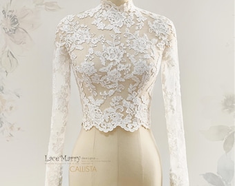 May include: A white lace top with long sleeves and a high neckline. The intricate floral lace pattern covers the entire top, creating a delicate and elegant look. The top is displayed on a mannequin.