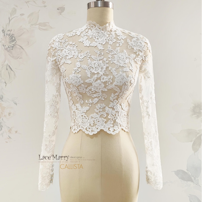 May include: A white lace top with long sleeves and a high neckline. The intricate floral lace pattern covers the entire top, creating a delicate and elegant look. The top is displayed on a mannequin.