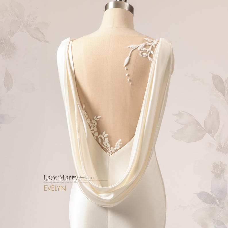 Pu&ograve; includere: Un abito da sposa in satin bianco con schiena scoperta e un pannello trasparente con ricami floreali delicati. L'abito ha una schiena drappeggiata a cappa.
