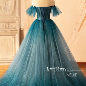 K&ouml;nnte beinhalten: Ein blaues T&uuml;ll-Ballkleid mit einem herzf&ouml;rmigen Ausschnitt und schulterfreien &Auml;rmeln. Das Kleid hat einen Schn&uuml;rr&uuml;cken und ist mit Glitzer verziert. Das Kleid wurde von Lace Marry entworfen und hei&szlig;t "Nellie".