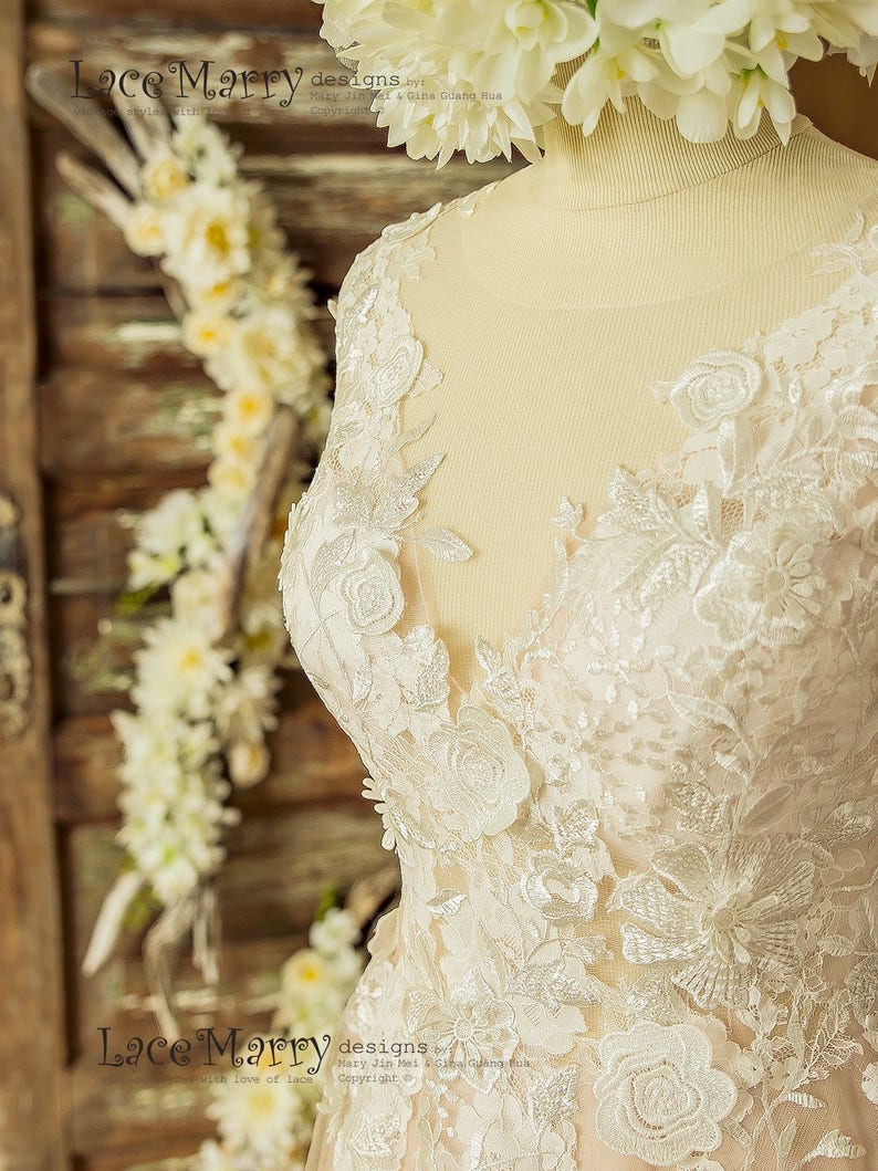 May include: Close-up of a white lace wedding dress with floral embroidery. The dress has a V-neckline and a fitted bodice. The lace is delicate and intricate, with a subtle shimmer.