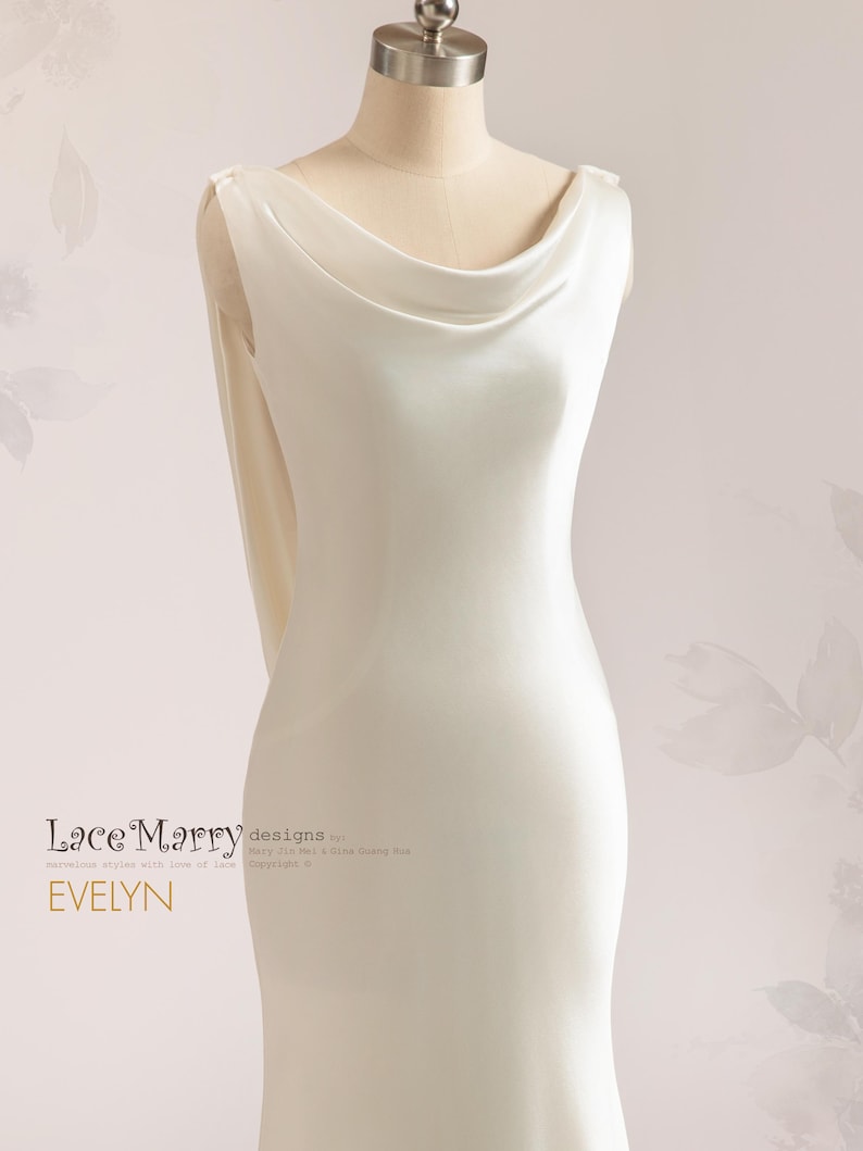 Pu&ograve; includere: Un abito da sposa bianco senza maniche in satin con scollo a barchetta e una lunga coda. L'abito &egrave; aderente e ha un design semplice. Il testo "Lace Marry designs" e "EVELYN" &egrave; visibile sull'abito.