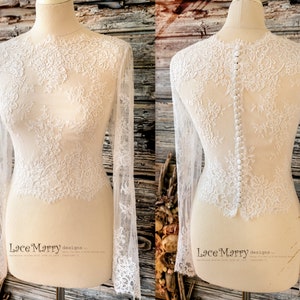 May include: White lace bridal top with long sleeves and a button fastening down the back. The top is sheer and features a delicate floral pattern.