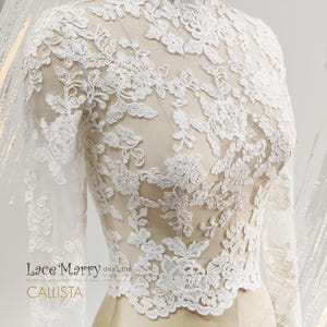 May include: A white lace top with long sleeves and a high neckline. The intricate floral lace design covers the entire top, creating a delicate and elegant look. The top is displayed on a mannequin, showcasing its form and details. The text "Lace Marry designs" and "CALLISTA" are visible.