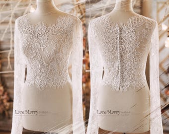 May include: A white lace bridal top with long sleeves and a button closure down the back. The lace has a floral pattern.