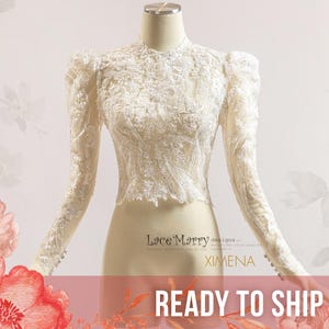 May include: Ivory lace top with long sleeves and a high neckline. The top features intricate floral lace detailing and puffed sleeves. The text "READY TO SHIP" is displayed on a red banner at the bottom of the image.