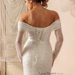 May include: A white off-the-shoulder wedding dress with long sleeves and a lace-up back. The dress is covered in sequins and has a fitted silhouette. The dress is designed by Lace Marry.