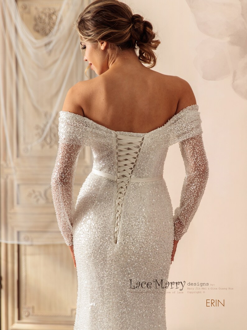 May include: A white off-the-shoulder wedding dress with long sleeves and a lace-up back. The dress is covered in sequins and has a fitted silhouette. The dress is designed by Lace Marry.