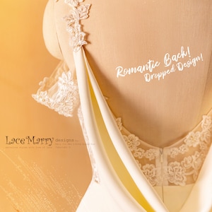 May include: A white wedding dress with a lace bodice and a draped back. The back of the dress has a romantic dropped design. The text "Romantic Back! Dropped Design!" is written on the dress.