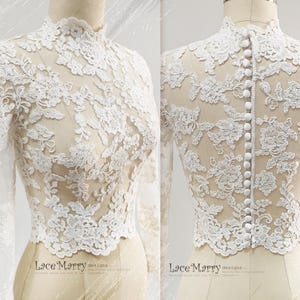May include: A white lace top with long sleeves and a high neckline. The intricate floral lace design covers the entire top, with a row of buttons down the back. The top is displayed on a mannequin.