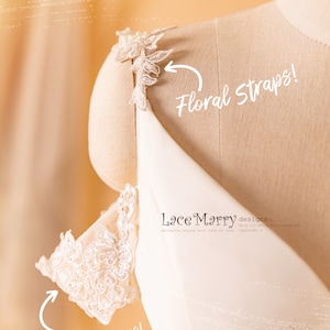 May include: A white off-the-shoulder dress with delicate lace straps. The straps are decorated with floral appliques. The dress is on a white mannequin. The text "Lace Marry designs" is visible on the dress.