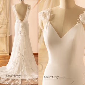 May include: A white wedding dress with a fitted bodice and a flowing skirt. The dress has a deep V-neckline and a low back. The skirt is adorned with delicate lace appliques. The dress is shown on a mannequin.