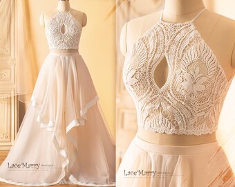 May include: A two-piece wedding dress with a white lace halter top and a flowing, layered tulle skirt in a light beige color. The top features a keyhole cutout in the front and delicate floral lace patterns. The skirt has a ruffled, asymmetrical hemline.