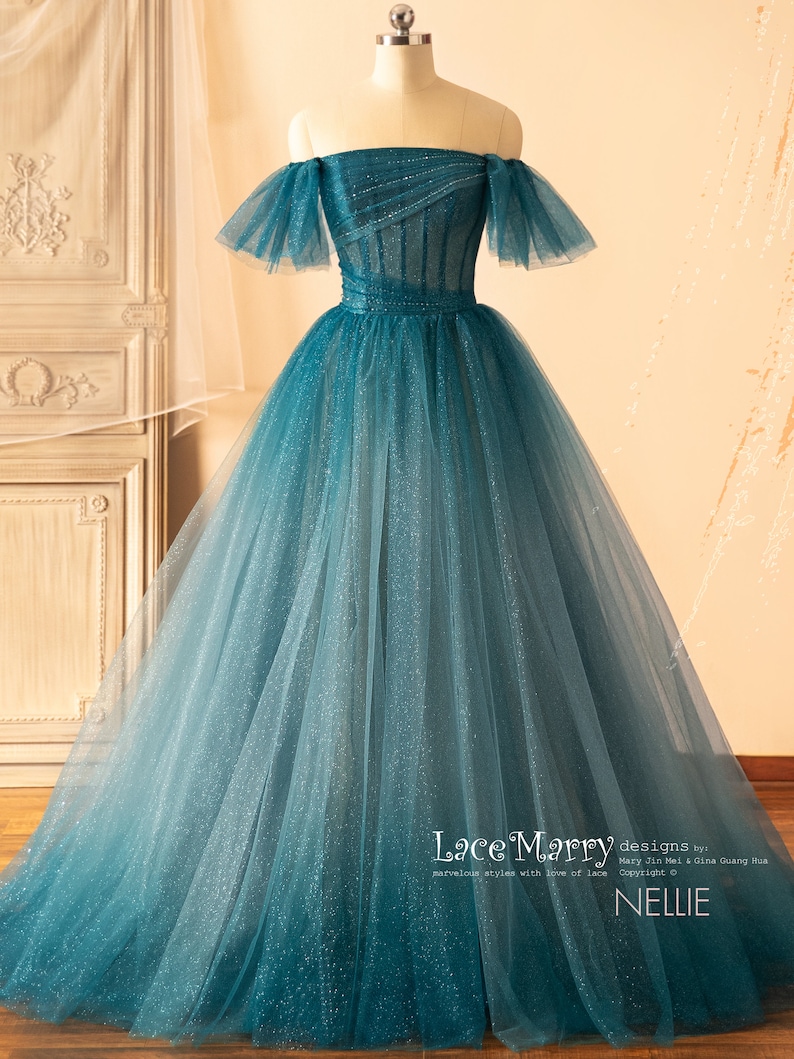 K&ouml;nnte beinhalten: Ein t&uuml;rkisfarbenes T&uuml;ll-Ballkleid mit einem herzf&ouml;rmigen Ausschnitt und abfallenden, schulterfreien &Auml;rmeln. Das Kleid ist mit Pailletten verziert und hat ein tailliertes Oberteil. Der Rock ist voll und flie&szlig;end. Das Kleid wurde von Lace Marry entworfen und hei&szlig;t "Nellie".