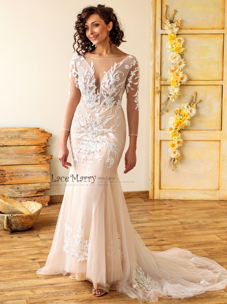 May include: A fitted, ivory wedding dress with a sheer bodice and long sleeves. The dress features intricate floral lace detailing and a flowing train.