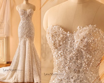 May include: A strapless, beaded wedding dress with a fitted bodice and a mermaid skirt. The dress is made of a sheer fabric with a delicate floral pattern and is adorned with sparkling sequins and beads.