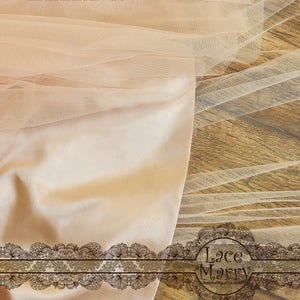 May include: A close-up of a piece of beige tulle fabric with a delicate lace trim. The fabric is draped over a wooden surface. The text "Lace Marry designs by Mary Jin Mei & Gina Guang Hua vintage styles with love of lace Copyright o" is visible in the top left corner of the image. The text "Lace Marry lacematty.etsy.com" is visible in the bottom right corner of the image.