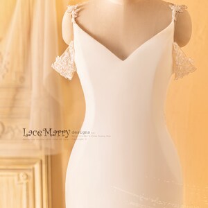 May include: A white off-the-shoulder wedding dress with lace detailing on the straps and sleeves. The dress has a fitted bodice and a flowing skirt. The dress is displayed on a mannequin against a light orange background. "Lace Marry designs by: Mary Jin Mei & Gina Quang Hua Copyright &copy;"