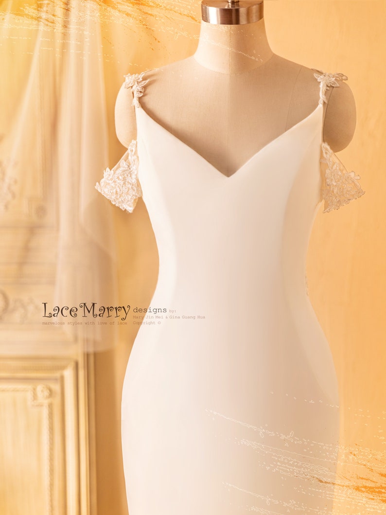 May include: A white off-the-shoulder wedding dress with lace detailing on the straps and sleeves. The dress has a fitted bodice and a flowing skirt. The dress is displayed on a mannequin against a light orange background. "Lace Marry designs by: Mary Jin Mei & Gina Quang Hua Copyright &copy;"