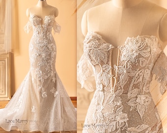 Può includere: Un abito da sposa bianco con scollatura a barca e un corpetto aderente e una gonna fluida. L'abito è ricoperto di pizzo floreale delicato e paillettes.