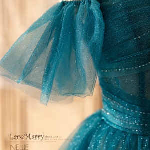 K&ouml;nnte beinhalten: Ein t&uuml;rkisfarbenes T&uuml;llkleid mit glitzerndem Finish und schulterfreien &Auml;rmeln. Das Kleid hat einen gerafften R&uuml;schen-Detail an den Schultern. Das Kleid hei&szlig;t "Nellie" von Lace Marry designs.