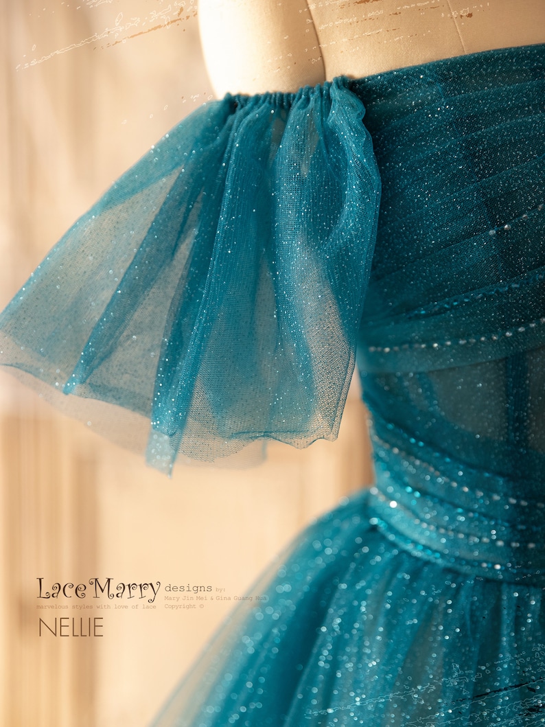 K&ouml;nnte beinhalten: Ein t&uuml;rkisfarbenes T&uuml;llkleid mit glitzerndem Finish und schulterfreien &Auml;rmeln. Das Kleid hat einen gerafften R&uuml;schen-Detail an den Schultern. Das Kleid hei&szlig;t "Nellie" von Lace Marry designs.