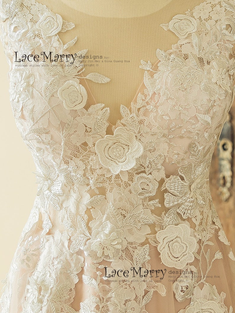 May include: A close-up of a white lace wedding dress with floral embroidery. The lace is delicate and intricate, with a variety of floral patterns. The dress is designed with a V-neckline and a fitted bodice. The text "Lace Marry designs" is visible on the dress.