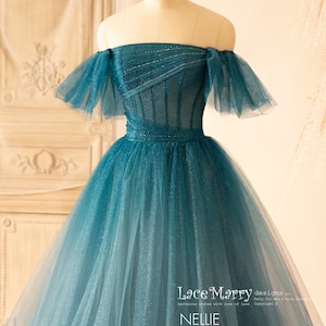 K&ouml;nnte beinhalten: Ein blaues T&uuml;ll-Ballkleid mit offener Schulter, einem figurbetonten Oberteil und einem vollem Rock. Das Oberteil ist mit Pailletten verziert und der Rock hat einen Farbverlauf, der von einem dunkleren Blau an der Oberseite zu einem helleren Blau an der Unterseite &uuml;bergeht. Das Kleid wurde von Lace Marry entworfen.