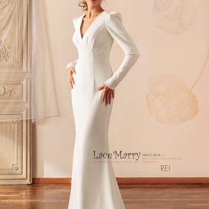 May include: A white long-sleeved wedding dress with a V-neckline and a fitted silhouette. The dress has a slight puff at the shoulders and a flowing train.