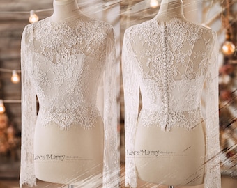 May include: A white lace bridal top with long sleeves and a button closure down the back. The top is made of delicate lace with a floral pattern. The top is shown on a white mannequin.