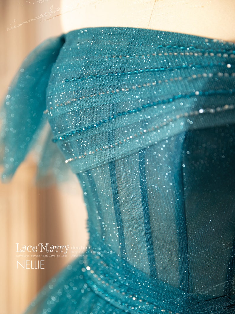 K&ouml;nnte beinhalten: Ein t&uuml;rkisfarbenes T&uuml;llkleid mit einem tr&auml;gerlosen Oberteil und einem glitzernden, perlenbesetzten Design. Das Kleid hat ein figurbetontes Oberteil und einen flie&szlig;enden Rock.