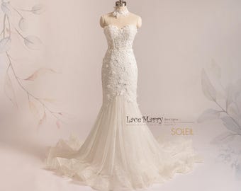 May include: A white, strapless wedding dress on a mannequin. The dress features intricate lace detailing on the bodice and a mermaid silhouette with a flowing tulle skirt. A matching lace choker is around the mannequin's neck. The dress is displayed against a soft, neutral background.