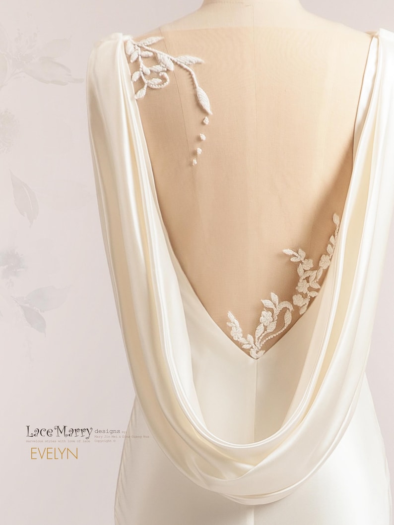Pu&ograve; includere: Un abito da sposa in satin bianco con schiena scoperta e un pannello trasparente con delicati ricami di pizzo floreale. L'abito ha una schiena drappeggiata a scialle.