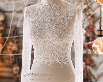 Op de afbeelding: Een wit kant bruidsjurk top met lange mouwen en een hoge halslijn. De kant heeft een bloemenpatroon en is zeer delicaat. De top is op een wit mannequin. De tekst "Lace Marry designs" en "MAGNOLIA #4" is afgedrukt op de onderkant van de afbeelding.