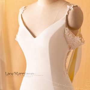 May include: A white wedding dress with a V-neckline and lace straps. The dress has a fitted bodice and a flowing skirt. The dress is on a mannequin.