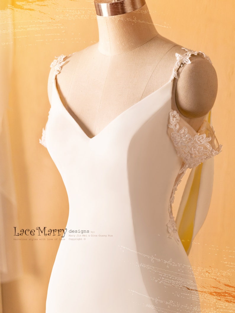 May include: A white wedding dress with a V-neckline and lace straps. The dress has a fitted bodice and a flowing skirt. The dress is on a mannequin.