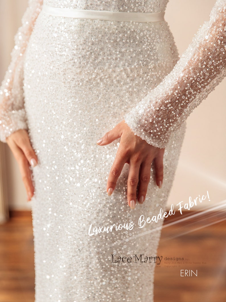 May include: A white beaded gown with long sleeves. The gown is covered in small, white beads that create a shimmering effect. The text "Luxurious Beaded Fabric!" is written on the gown. The text "Lace Marry designs" is written on the bottom of the gown.