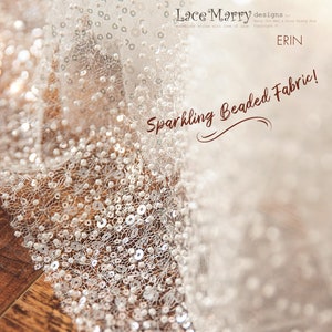 May include: Close-up of a white beaded fabric with a delicate lace pattern. The fabric is shimmering and has a subtle sparkle. The text "Lace Marry designs" and "Sparkling Beaded Fabric!" is visible in the image.