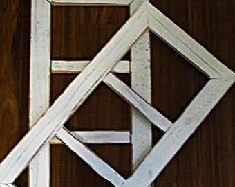 May include: Two white wooden picture frames with a criss-cross pattern, overlapping each other. The frames are on a brown wooden background.